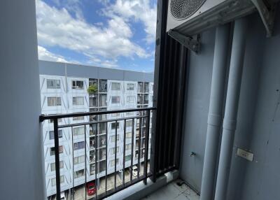 View of a balcony with a railing and an air conditioner unit, showing an apartment building across the street