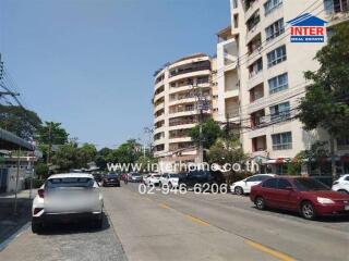 Street view of a multi-story residential building with cars parked on the street