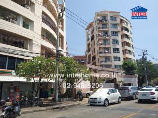 Front view of residential buildings on a street with parked cars and a convenience store