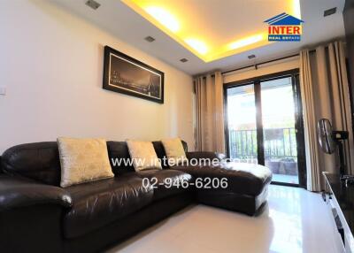 Modern living room with L-shaped leather sofa, decorative ceiling lighting, and balcony access.