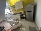 Modern kitchen with yellow accent wall, cabinets, appliances, and stairwell