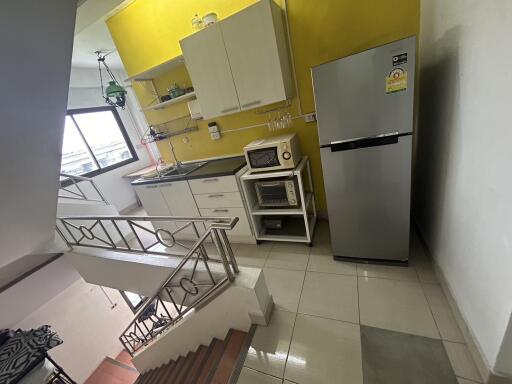 Modern kitchen with yellow accent wall, cabinets, appliances, and stairwell