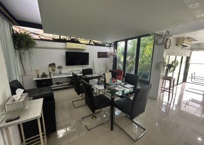 Modern living and dining area with glass table and black chairs, adjacent to a large window providing natural light.