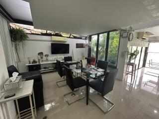 Modern living and dining area with glass table and black chairs, adjacent to a large window providing natural light.