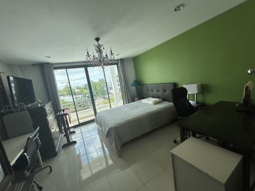 Spacious bedroom with a large window offering a view, featuring a chandelier, bed, desk, and a TV stand