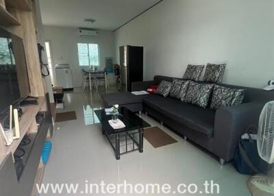 Modern living room with couch, wall-mounted shelves, and visible kitchen area in the background.