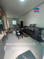 Modern living room with couch, wall-mounted shelves, and visible kitchen area in the background.