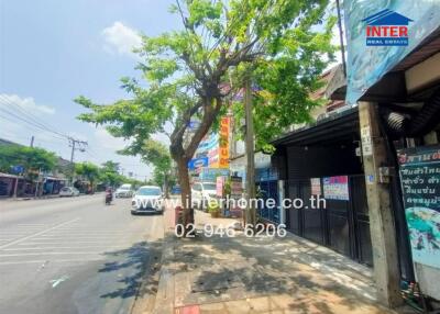 Street view in front of real estate property with a tree, cars, and shops.