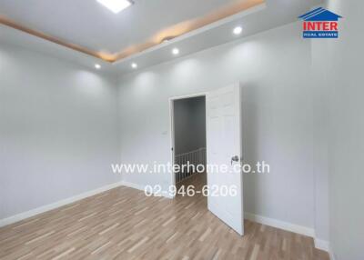 Empty bedroom with wooden floor and white walls, featuring a partially open white door.