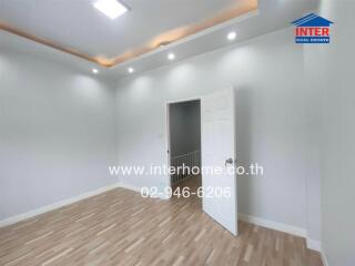 Empty bedroom with wooden floor and white walls, featuring a partially open white door.