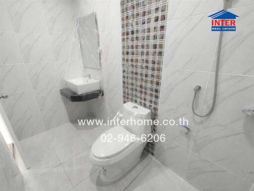 Modern bathroom with wall tiles, toilet, sink, mirror, and showerhead