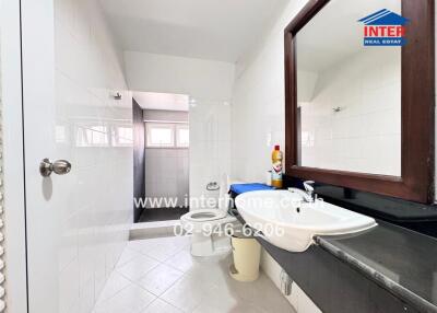 Bathroom with white tiles, a sink, mirror, toilet, and shower area.