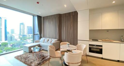 Modern living room with a view of the city skyline, featuring a seating area, dining table, and an adjacent kitchen.