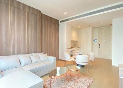 Modern living room with wooden wall paneling, light-colored furniture, and small dining area