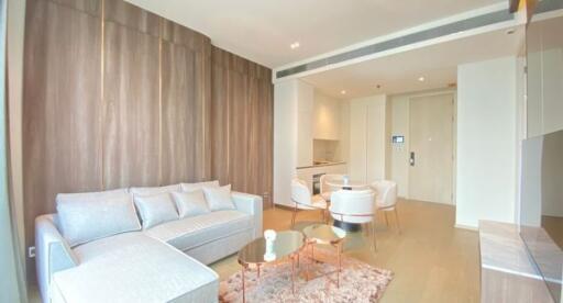 Modern living room with wooden wall paneling, light-colored furniture, and small dining area