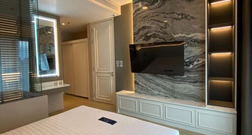 Bedroom with modern decor, featuring a wall-mounted TV and a stylish marble accent wall.