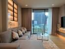 Modern living room with large windows, grey sofa, glass coffee table, wall-mounted TV, and city view.