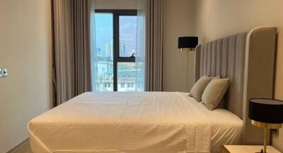 Bedroom interior with a bed, bedside tables and lamps, and a large window with city view.