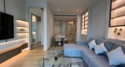 Modern living room with a stylish sofa, wall-mounted TV, and a view into a dining area and hallway