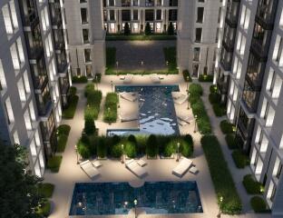 Aerial view of a modern apartment complex with illuminated windows, landscaped gardens, and two swimming pools.