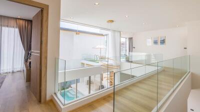 Modern hallway with wooden floors, glass railings, and view of lower level with pool