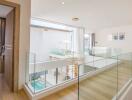 Modern hallway with wooden floors, glass railings, and view of lower level with pool