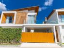 Modern two-story house exterior with a large wooden gate and lush greenery