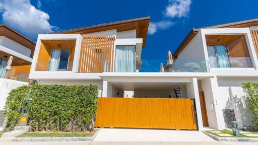 Modern two-story house exterior with a large wooden gate and lush greenery