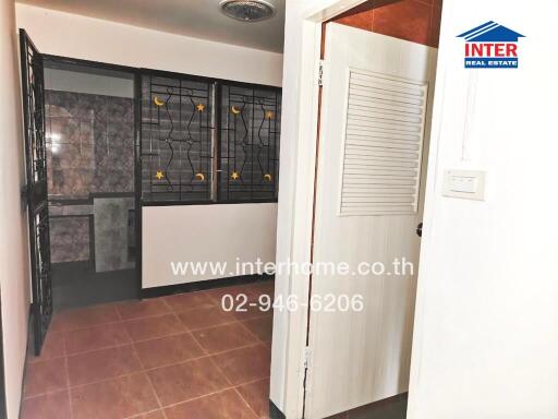 Photo of a room with tiled flooring, metal grill window and bathroom in the background