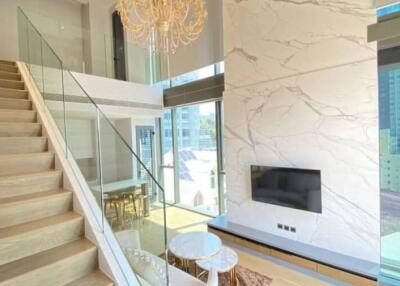 Modern living room with a staircase, chandelier, and large windows