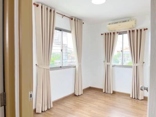 Bedroom with wooden flooring, white walls, and large windows covered by beige curtains