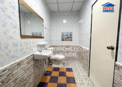 Bathroom with tiled walls, mirror, sink, toilet, and colorful mat