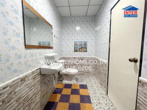 Bathroom with tiled walls, mirror, sink, toilet, and colorful mat