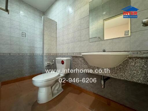 Modern bathroom with tiled walls and floor, featuring a toilet and a wall-mounted sink