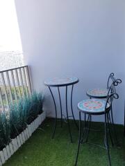 Cozy balcony with bar table and stools, green artificial grass, and decorative plants