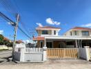 Two-story house with white fence and red roof under clear blue sky