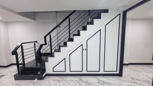 Modern staircase with sleek black railing and white storage cabinets beneath