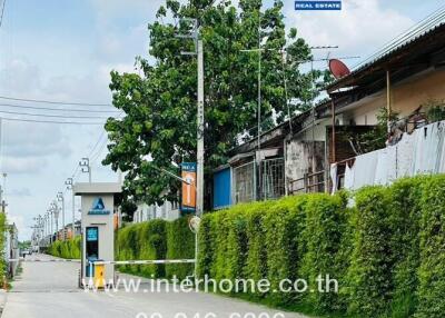 Entrance of residential area with tall green hedge, Inter Real Estate signboard, and road extending into the distance