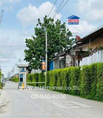 Entrance of residential area with tall green hedge, Inter Real Estate signboard, and road extending into the distance