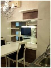 Modern living room with a dining table, chairs, wall-mounted TV, chandelier, and shelving