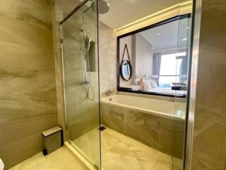 Modern bathroom with glass shower enclosure and bathtub with a view into the bedroom