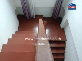 View of a staircase with brown steps and handrail, with curtains visible at the top of the stairs