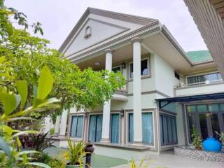 Front view of a two-story house with columns and surrounding garden