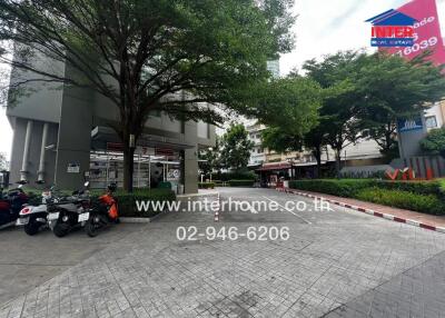 Entrance area of a building with trees, parked motorcycles, and a visible real estate sign