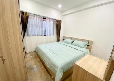 A cozy bedroom with a double bed, light wooden furniture, and large window with curtains.