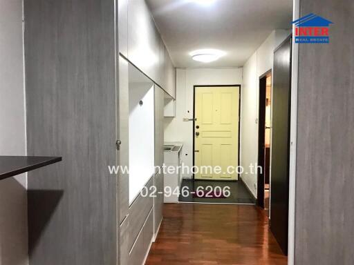 A hallway leading to a door with light gray and wooden paneling