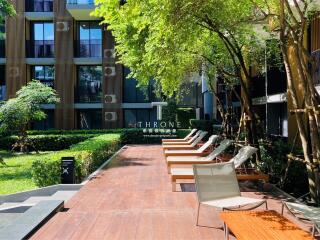 Modern outdoor communal area with lounge chairs and greenery, in front of an apartment building