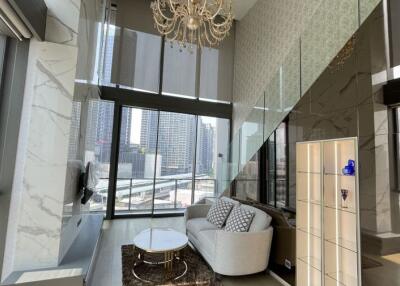 Modern living room with large windows, a couch, coffee table, chandelier, and city view
