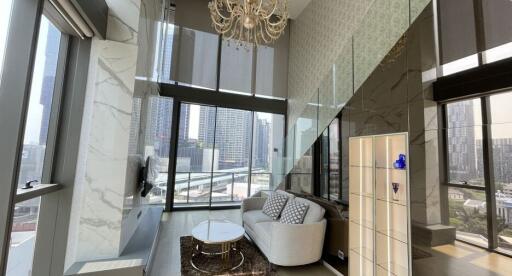 Modern living room with large windows, a couch, coffee table, chandelier, and city view