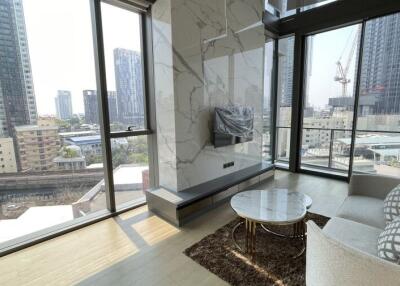 Modern living room with large windows, city view, marble accent wall, and a mounted television